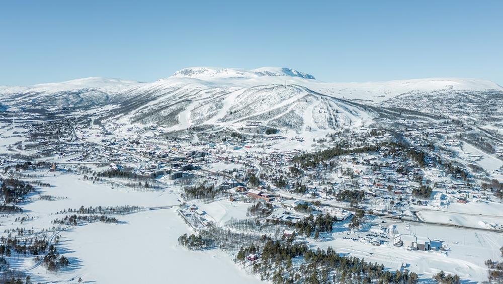 Luftfoto av snødekt Geilo sentrum og fjellene bak - Klikk for stort bilde