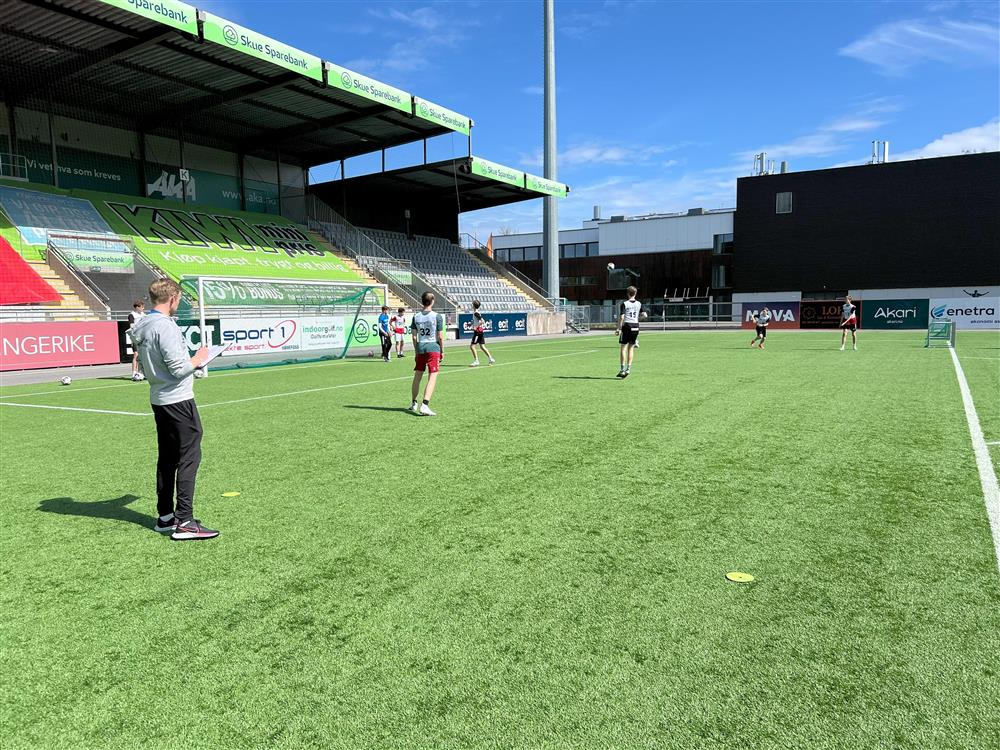 Flere som står og observerer noen som spiller fotball - Klikk for stort bilde